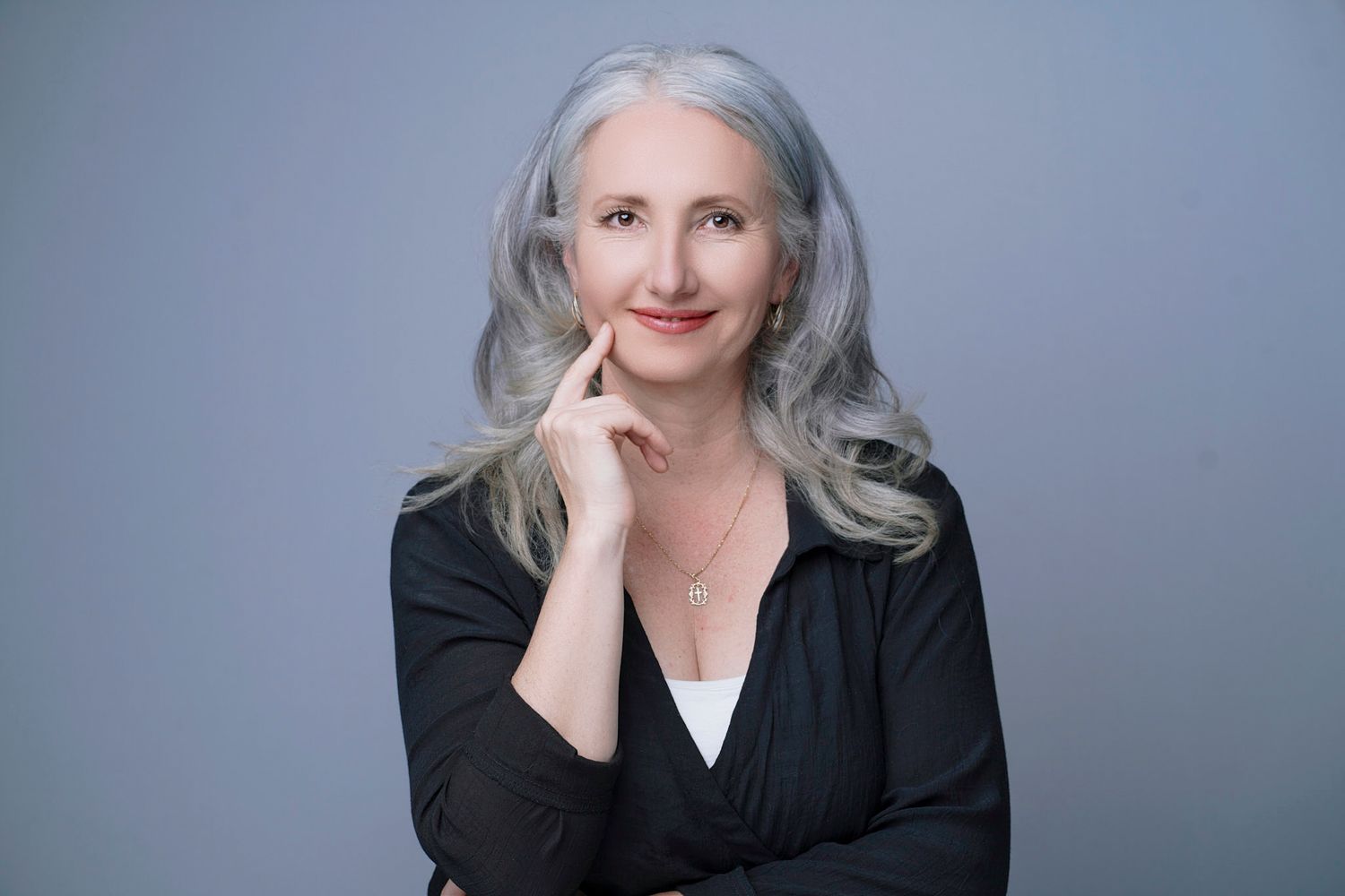 Professional portrait of Vear Spence with long silver hair wearing a black blazer against a gray background.
