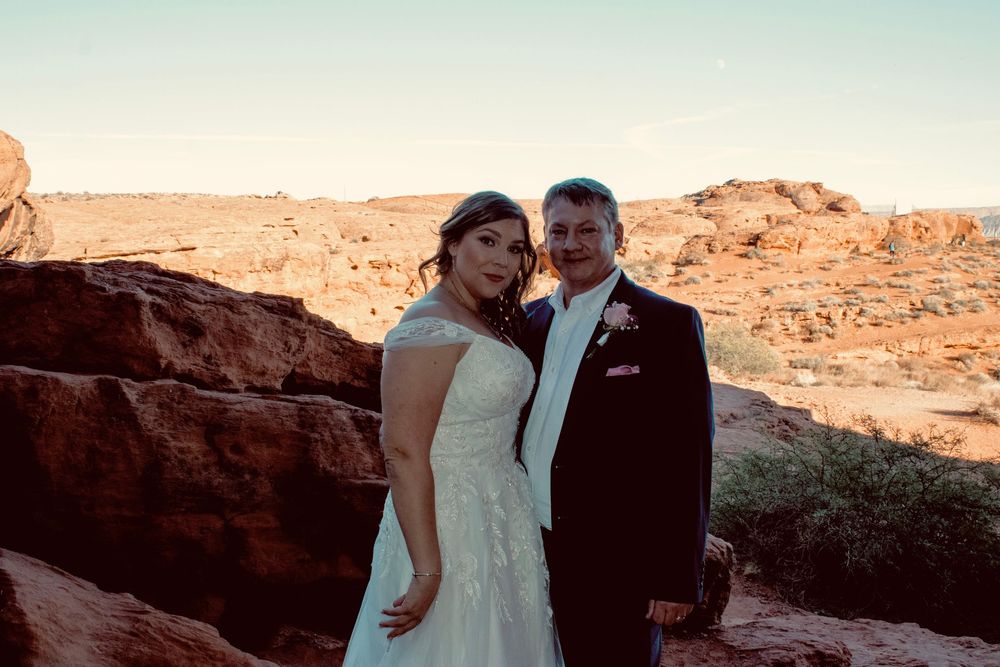 Bride and groom standing together smiling at red rock desert landscape during outdoor wedding.