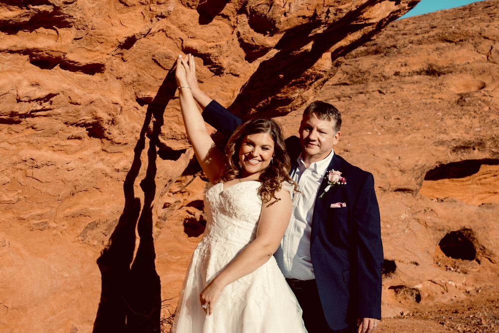 Joyful bride and groom posing playfully under natural rock arch at red rock canyon wedding.
