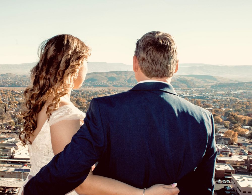 Wedding couple standing back to back overlooking scenic mountain city panorama together.