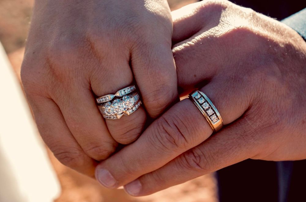 Close-up of newlyweds hands displaying sparkling diamond and turquoise wedding rings.