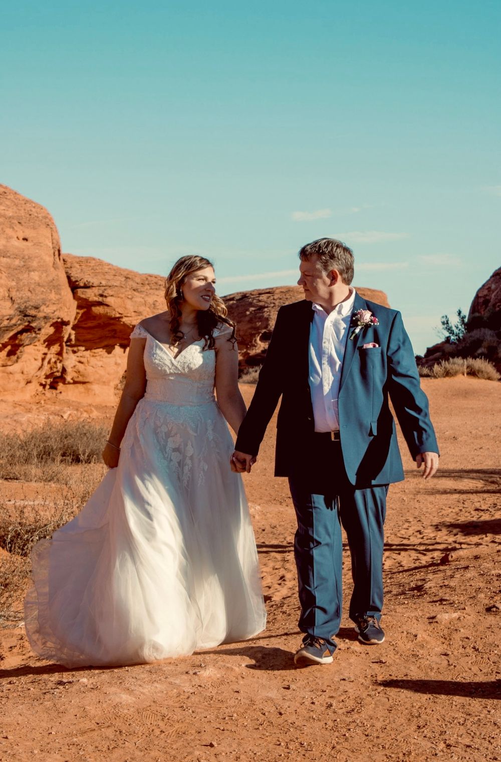 Bride and groom holding hands walking through red rock desert landscape on their wedding day.