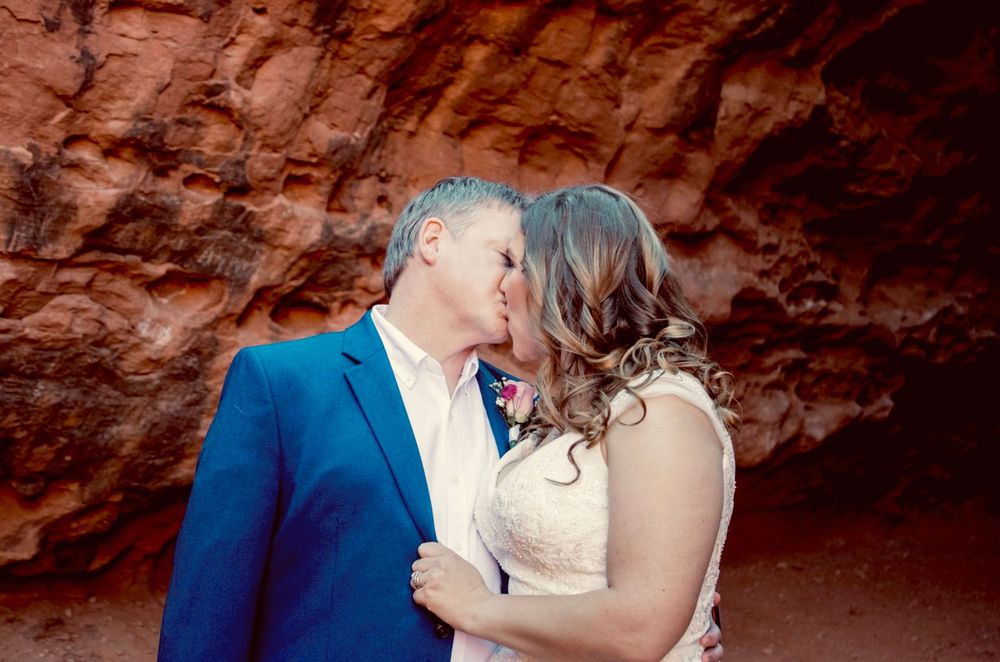 Bride and groom share a romantic kiss against stunning red rock canyon walls during their desert wedding.