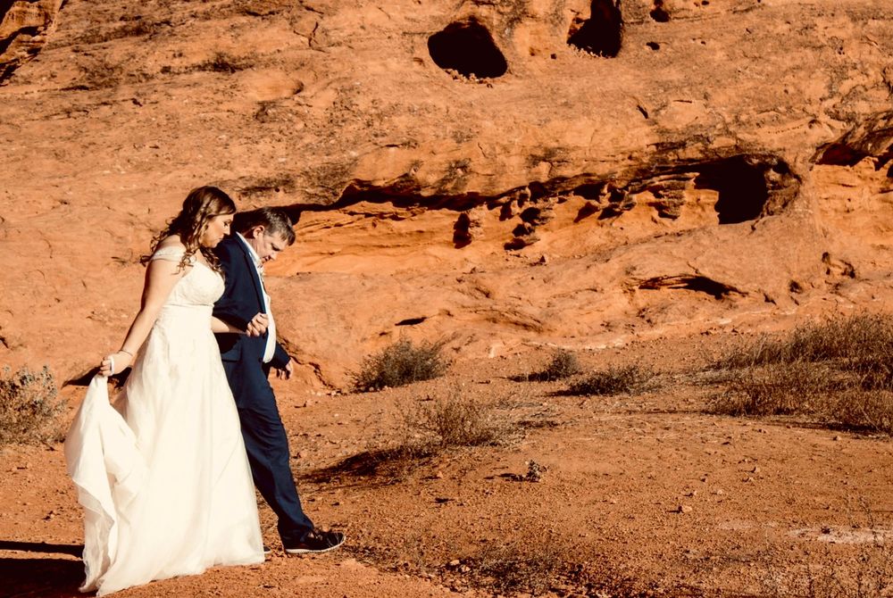 Bride and groom share an intimate moment among dramatic red rock formations in desert setting.