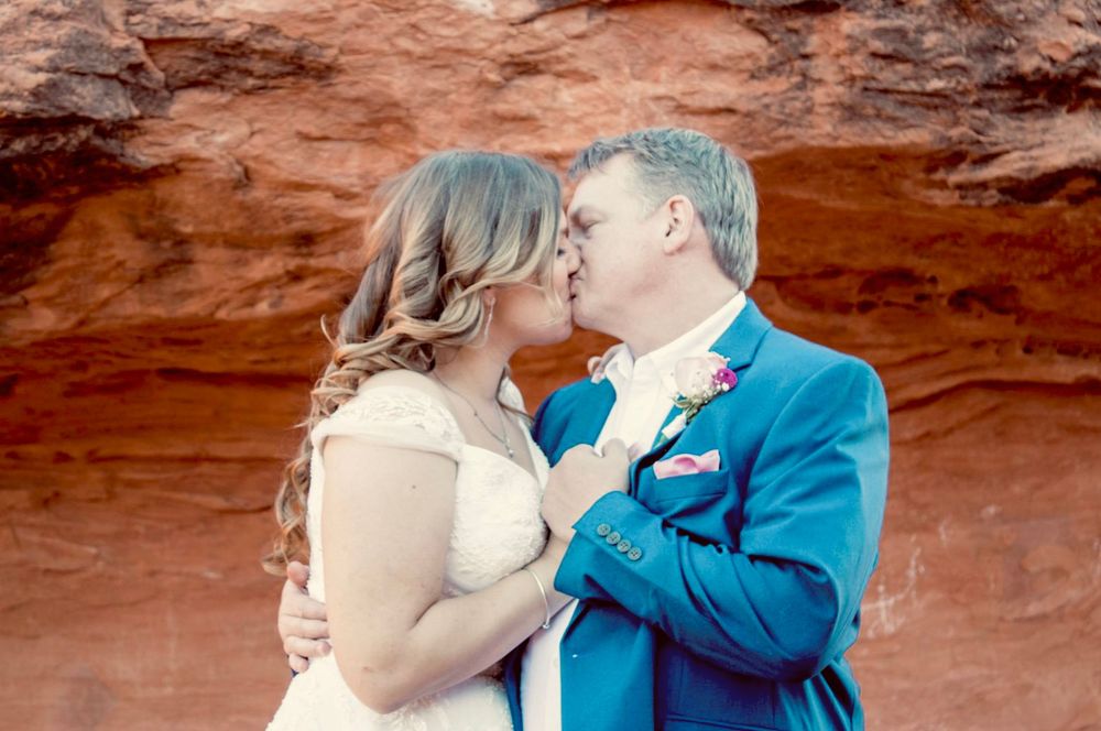 Bride and groom share a tender kiss against vibrant red sandstone rock wall at wedding.