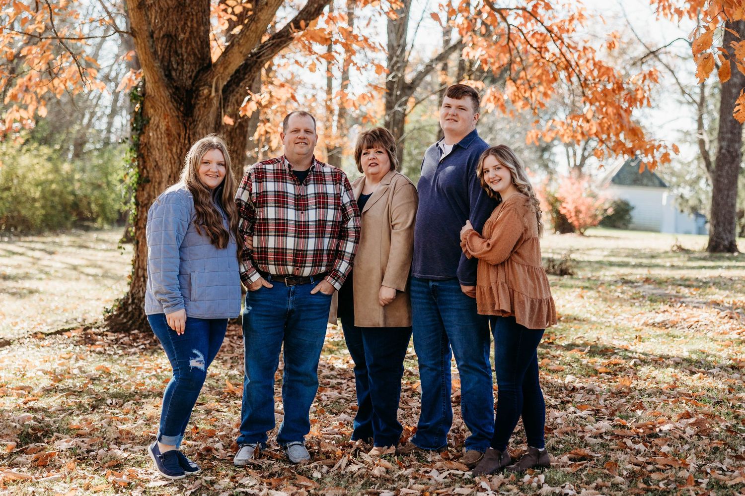 A multigenerational family group poses together under fall foliage.