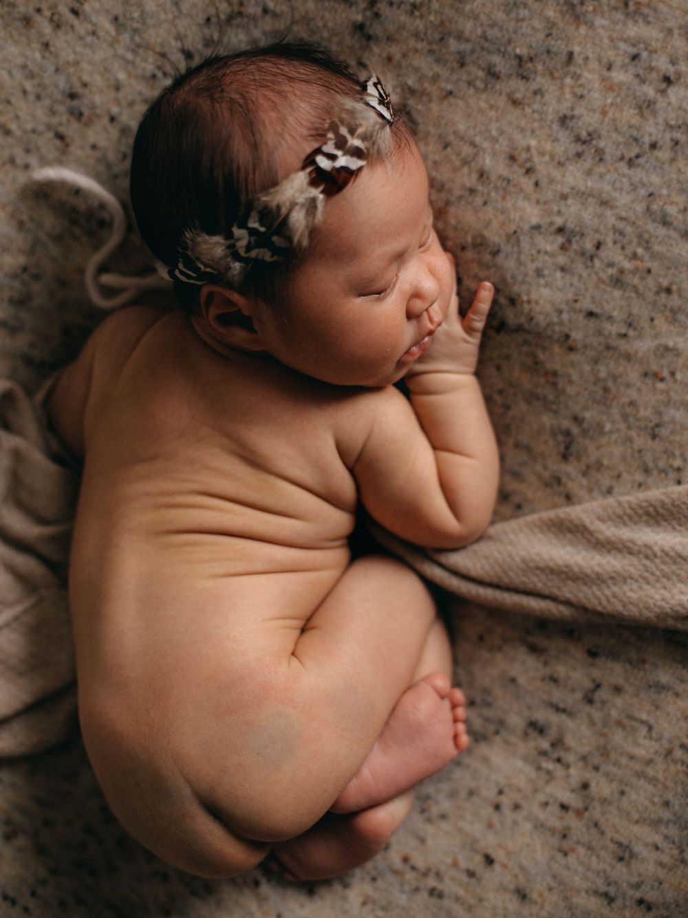 Newborn wearing delicate floral crown rests on textured beige backdrop during photo session.