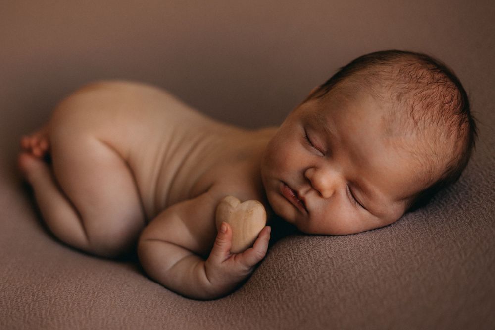 Peaceful sleeping newborn curled up on soft brown fabric during studio photography session.