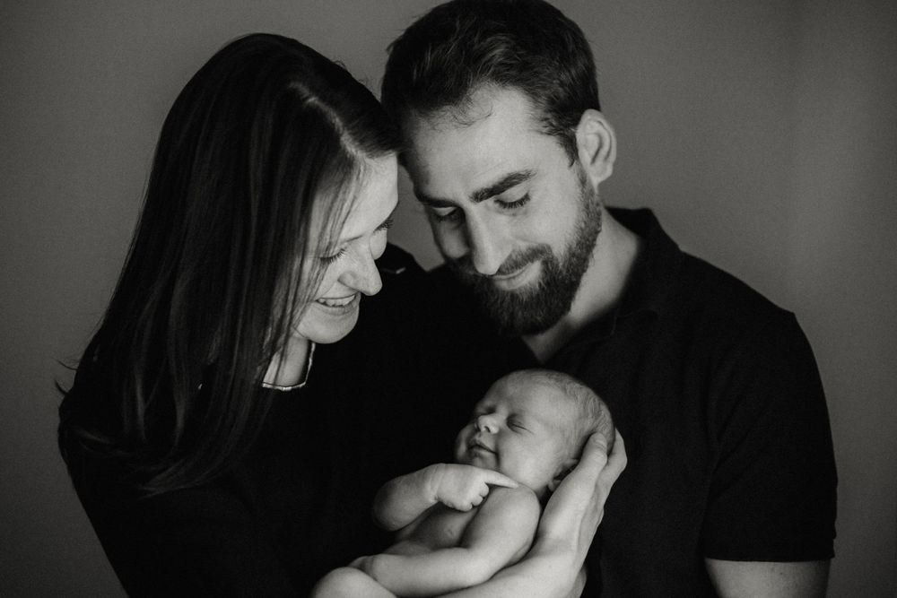 Intimate black and white family moment with newborn being held by loving parents.