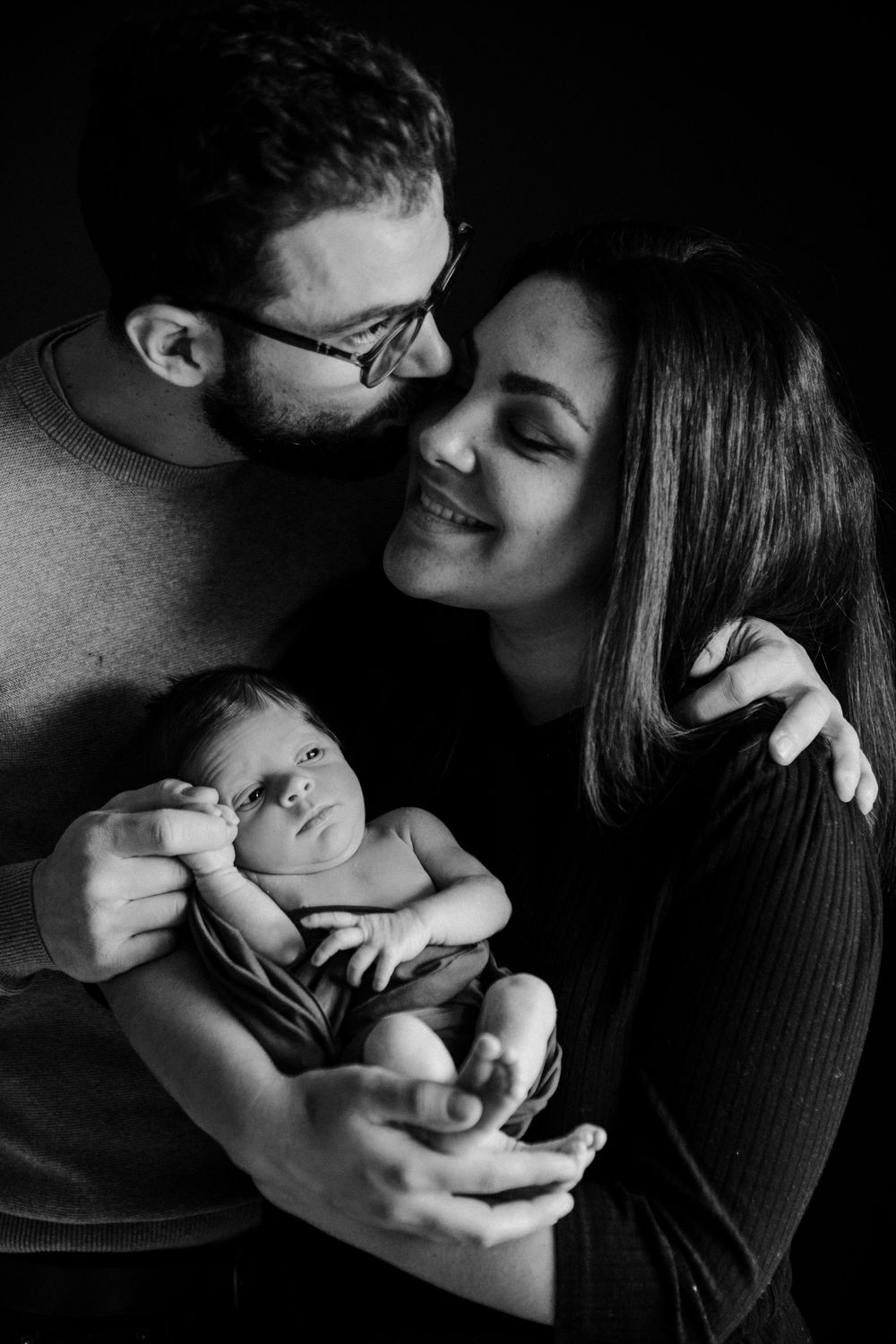 Intimate black and white family portrait with newborn nestled between parents.