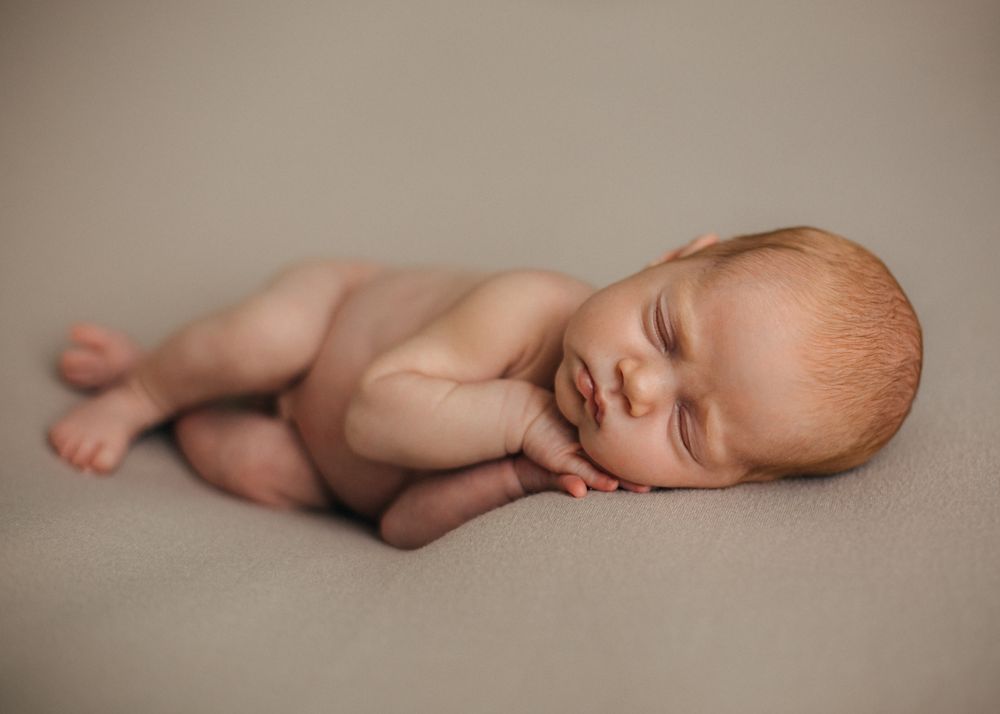 Sleeping newborn lying on side against neutral beige background in studio setting.