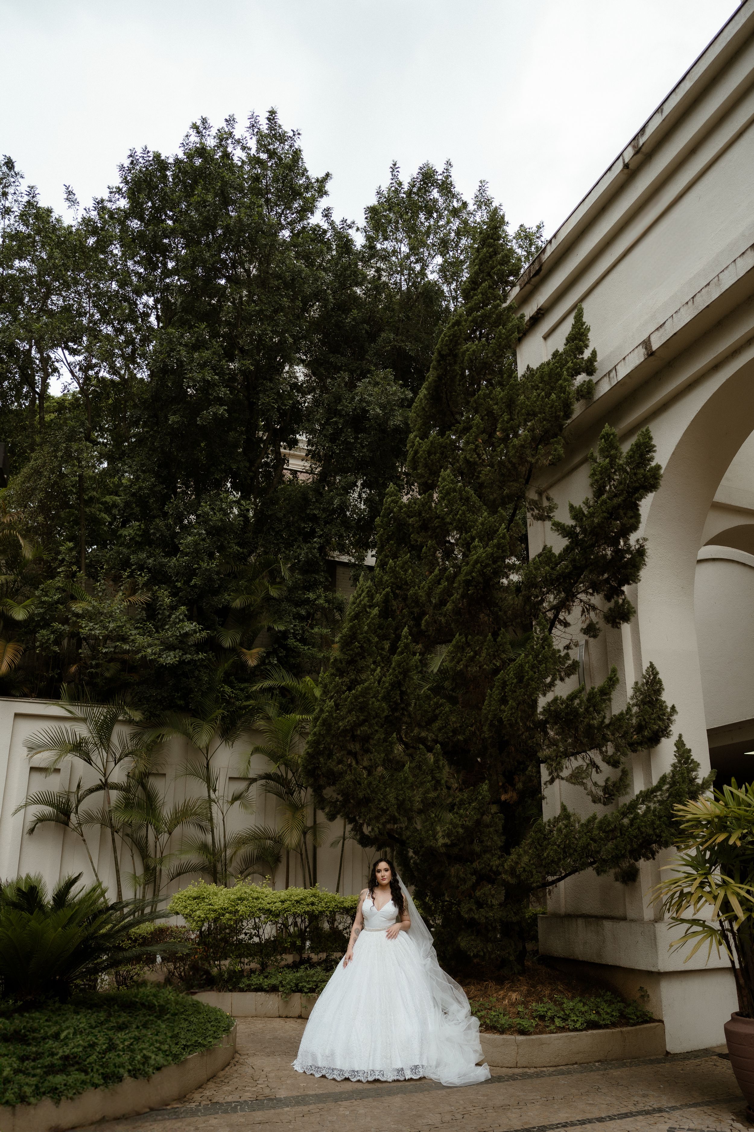 Wedding dress silhouette against classical architecture and lush garden backdrop.