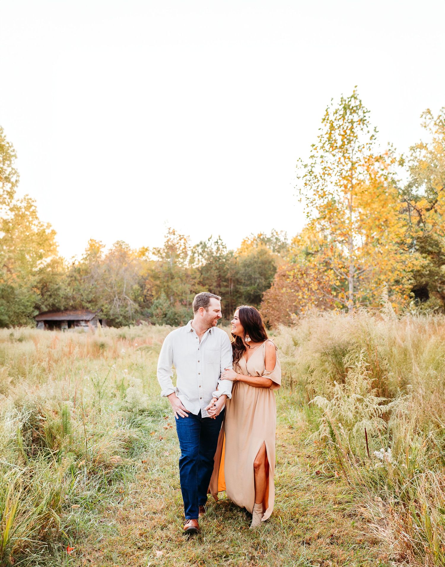 A couple walks together through a golden field at sunset during a romantic outdoor photoshoot.