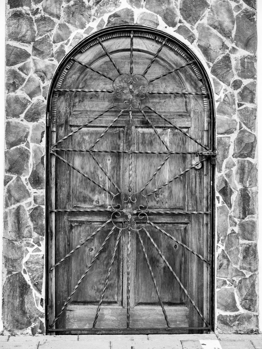 Black and white photo of an ornate arched wooden door set in stone wall.