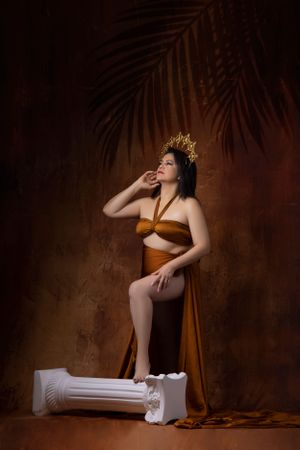 Artistic maternity portrait with gold crown against warm brown backdrop.