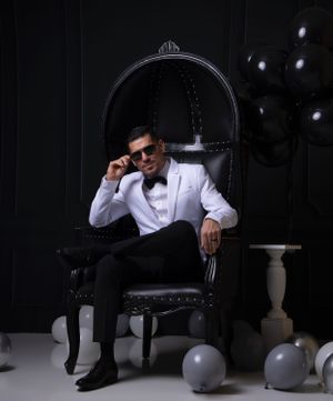 Stylish man in gray suit poses on vintage chair in dramatic dark studio setting.