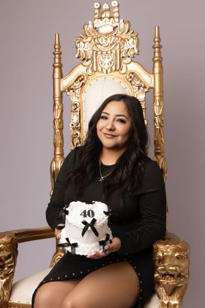 Professional portrait session on ornate gold throne chair against grey backdrop.