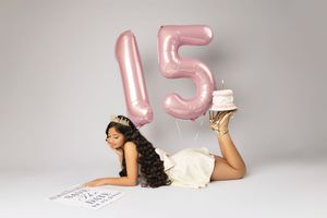 Pink number 15 balloons float against a light gray studio backdrop in a celebratory setup.