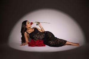 Elegant portrait with red roses in black lace dress against light backdrop.
