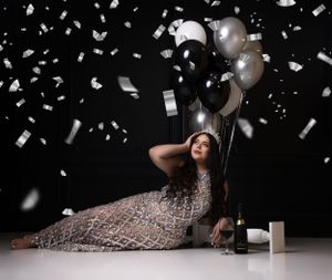 Glamorous portrait with silver balloons and confetti in sequined dress.