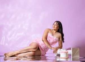 Romantic boudoir portrait in pink dress with cake props against pink background.