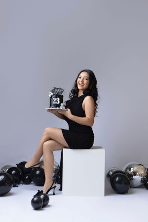 Birthday portrait session with black balloons and number cake on white platform.