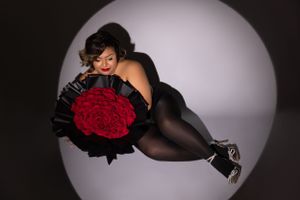 Glamorous maternity photoshoot featuring elegant black gowns and red roses against a dark background.