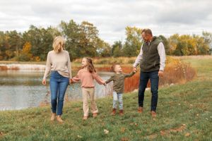 Family holding hands while walking near lake during autumn season.