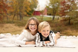Children laying on white blanket during fall photoshoot with rustic backdrop.