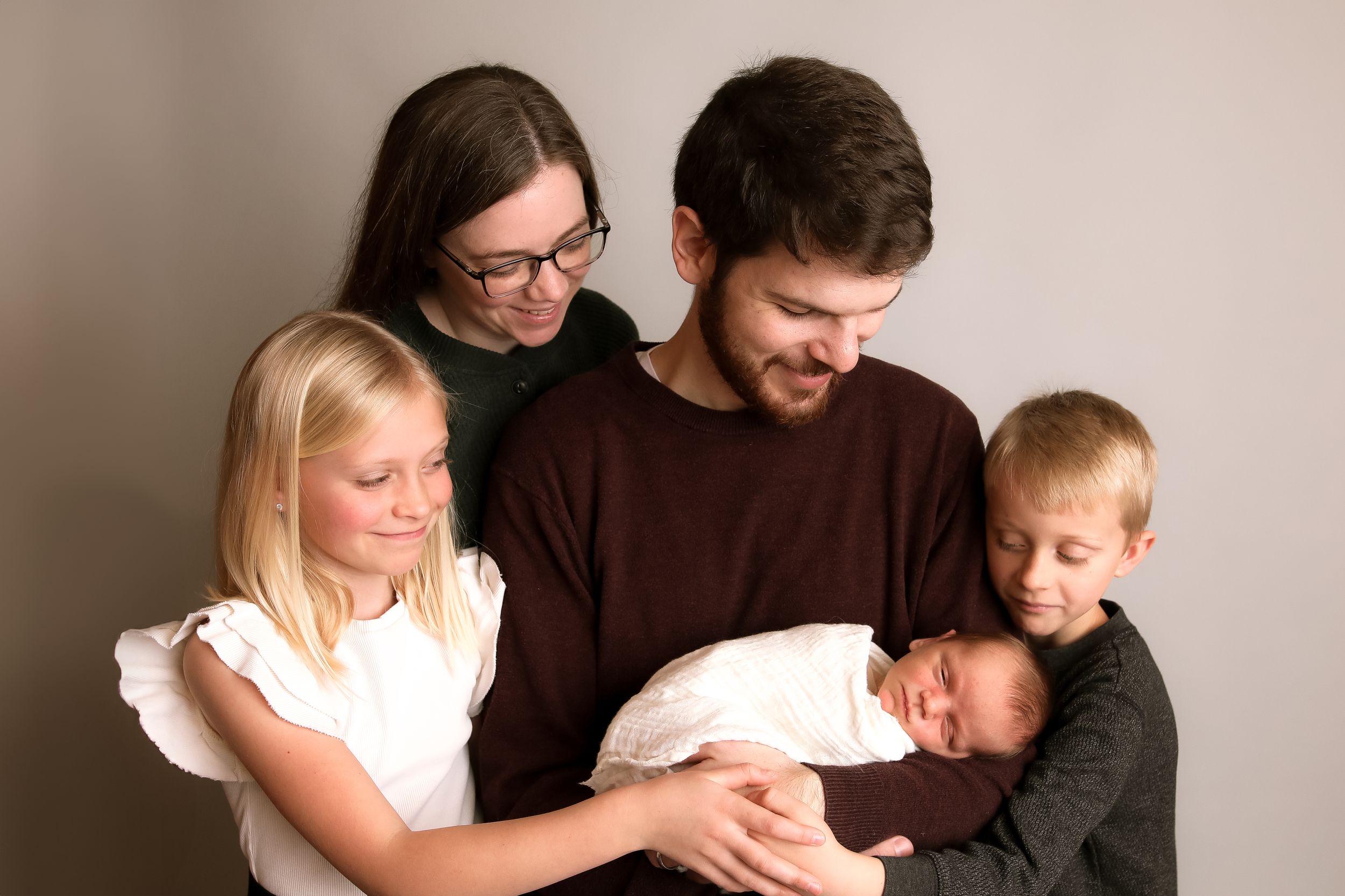 Studio portrait of a family of five with newborn baby in minimalist setting.