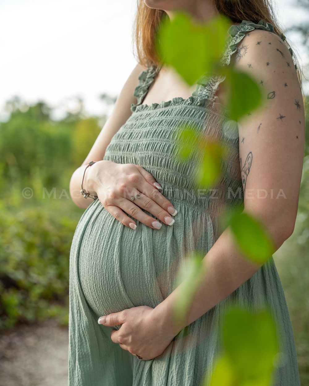 A maternity photo showing a sage green dress with delicate smocking details in an outdoor garden setting.