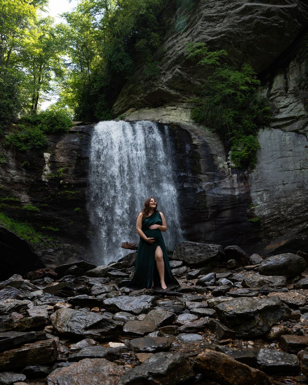 A pregnant woman poses for a maternity photoshoot under Looking Glass Falls in Brevard, North Carolina