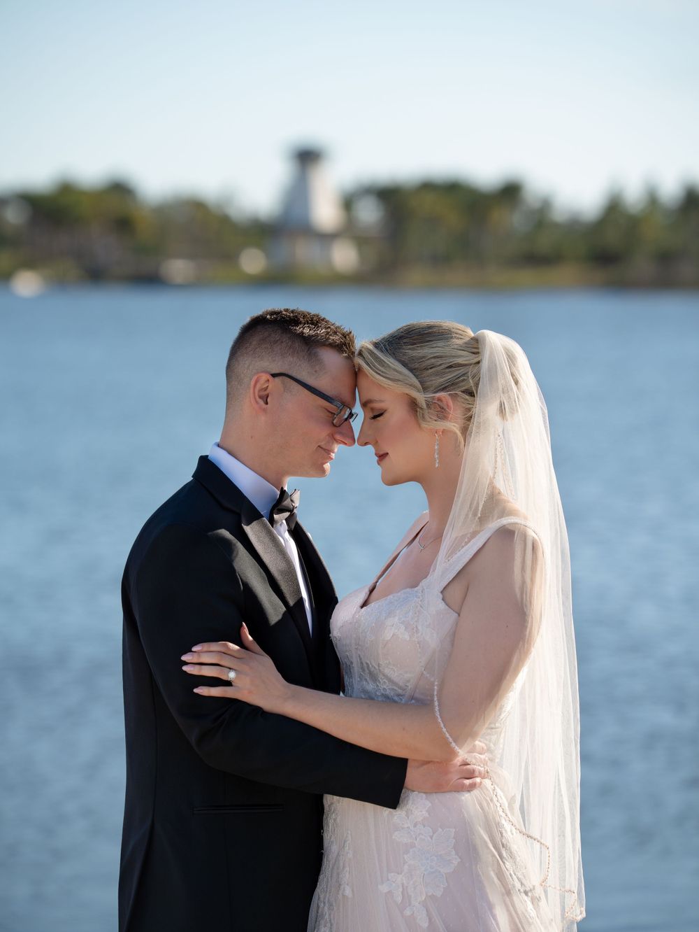 Romantic Venice Florida waterfront wedding portrait with couple embracing against blurred lighthouse background.