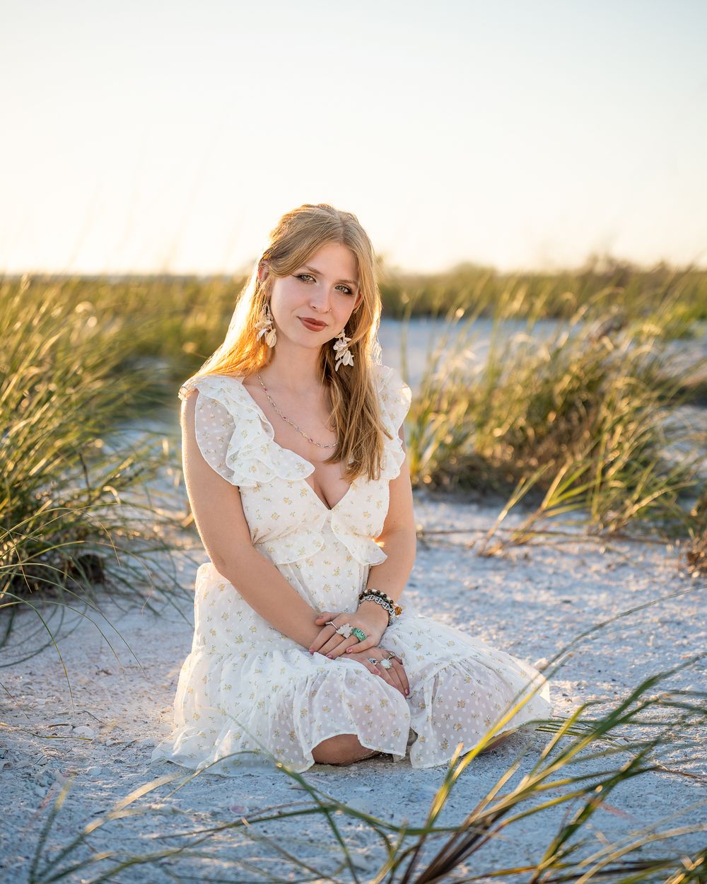 Woman in white dress sits gracefully for senior session photo on sandy beach dunes at Lido Beach in Sarasota Florida.