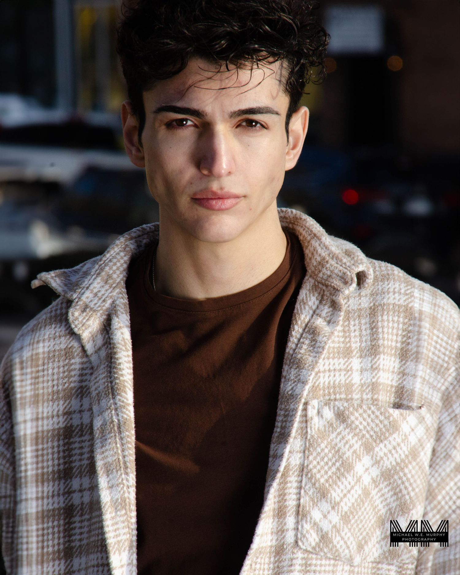 Casual outdoor portrait featuring person in brown shirt and plaid jacket.