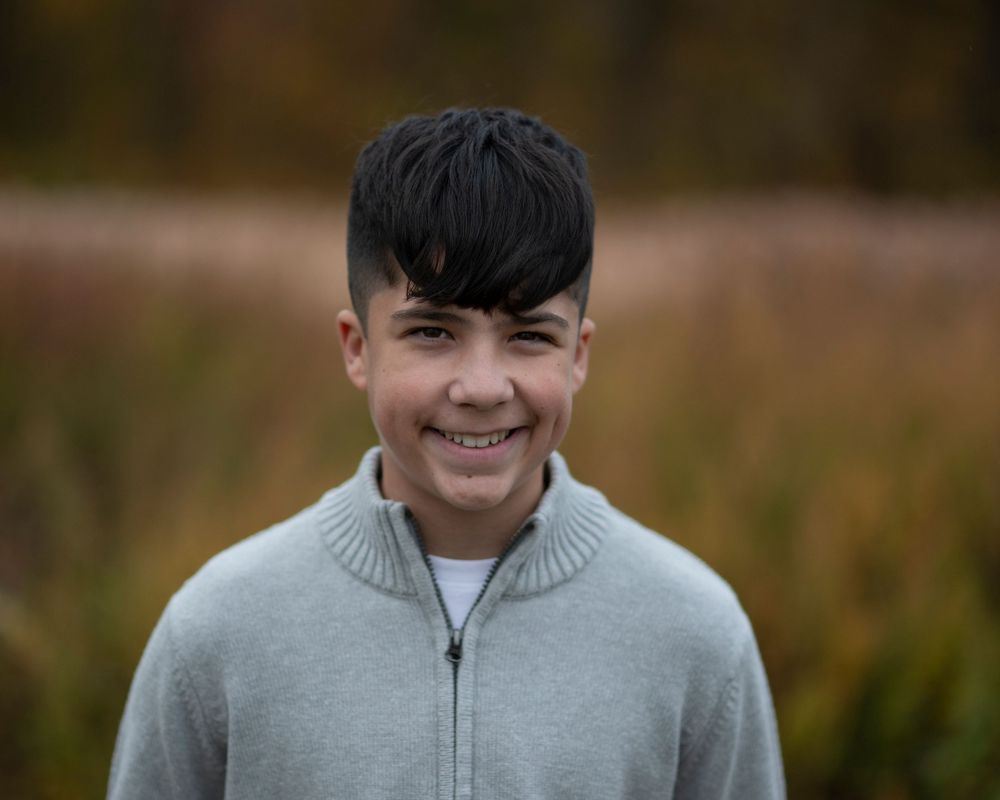 Child portrait of Happy young boy with dark hair wearing a gray zip-up sweater smiling outdoors in fall setting. Middletown NJ