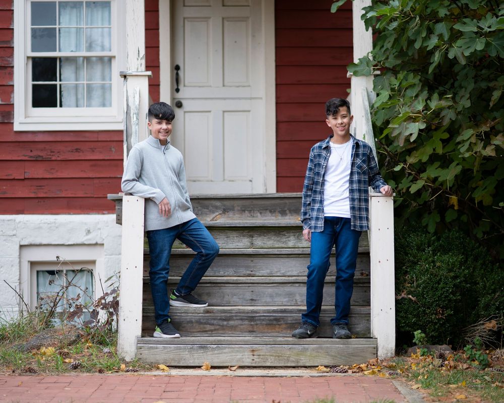 Two teenage boys standing on weathered porch steps of red house, posing casually outdoors in fall.Middletown NJ
