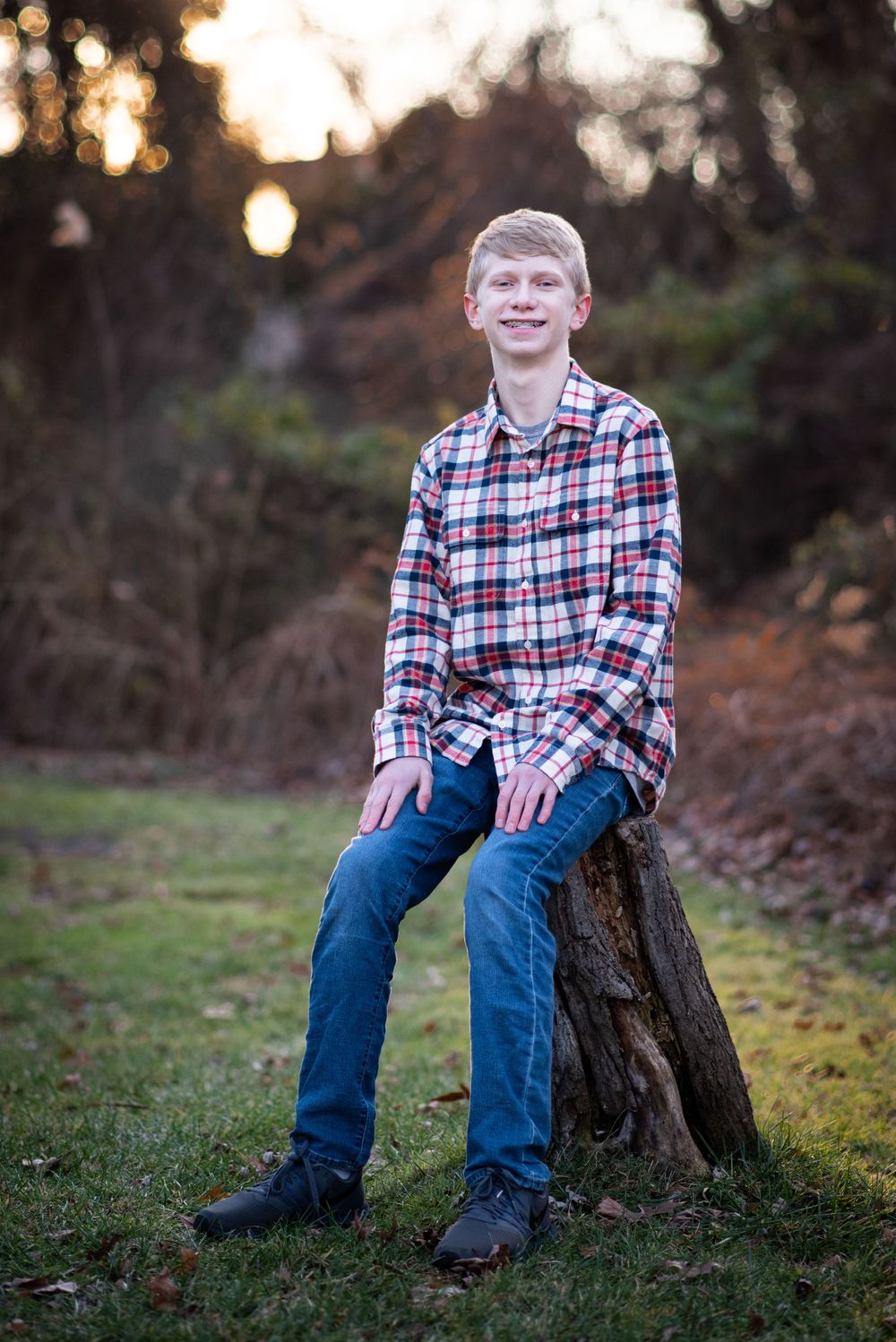portrait of teen boy in plaid shirt and jeans sitting on tree stump at sunset.Middletown NJ