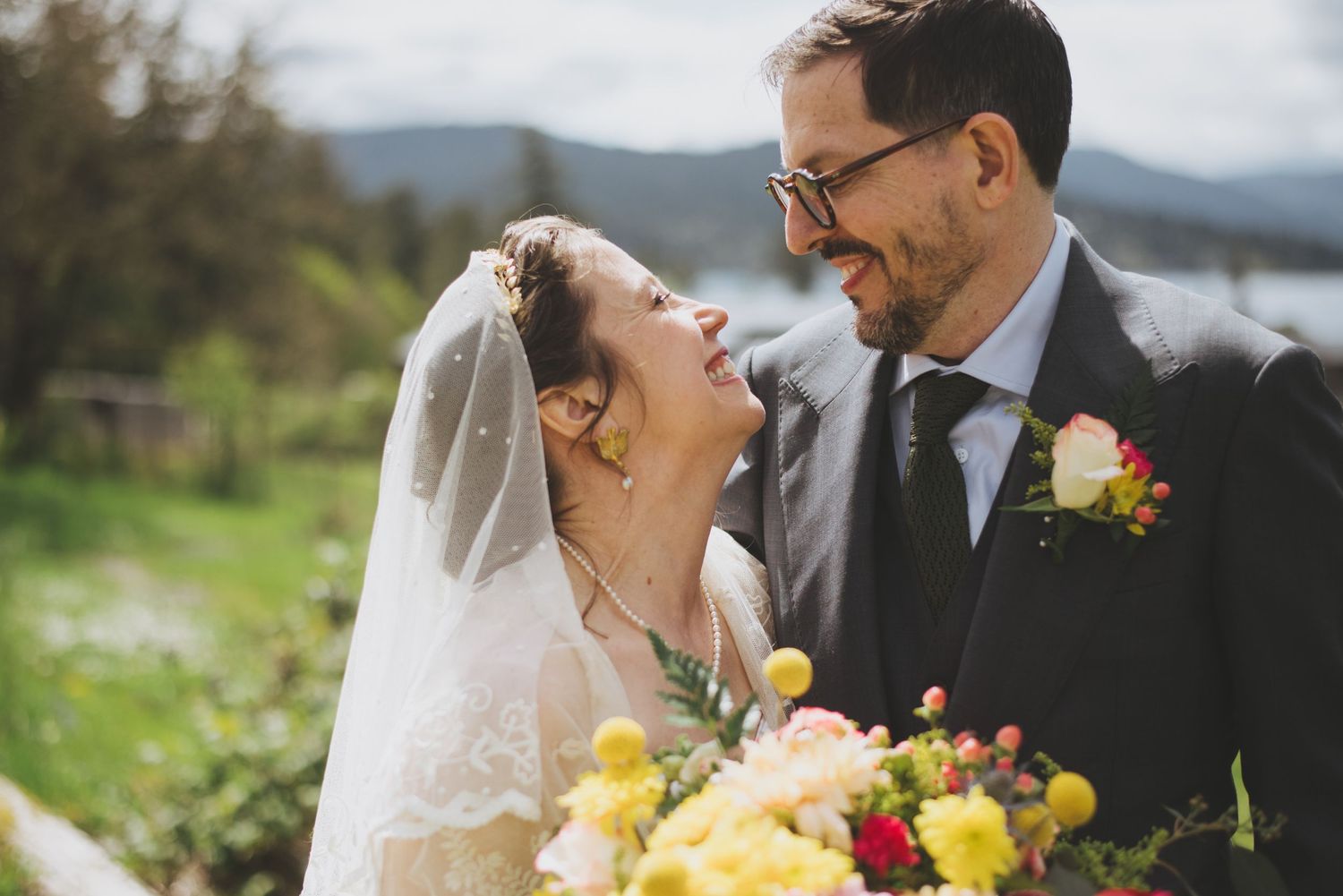 A happy couple share an intimate moment outdoors with yellow flowers and mountains in the background.