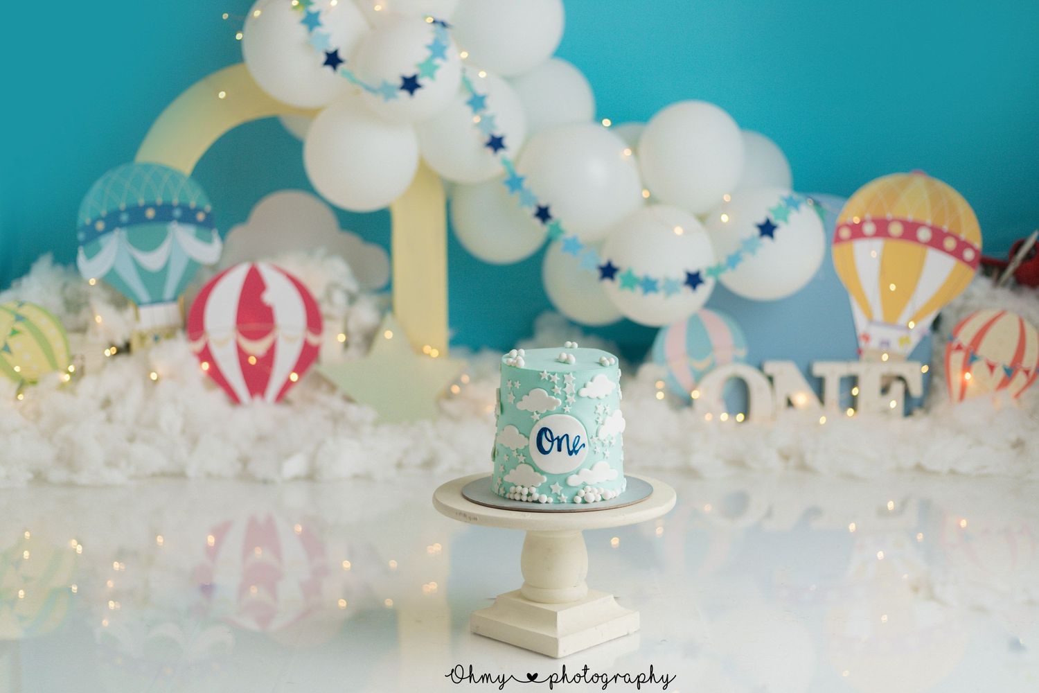 Hot air balloon themed cake display with white balloon arch and pastel decorations.