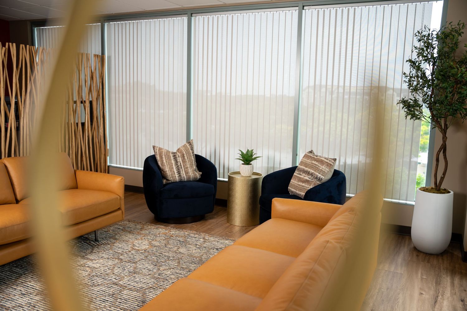 Modern living room interior with vertical blinds and orange couch near large windows.