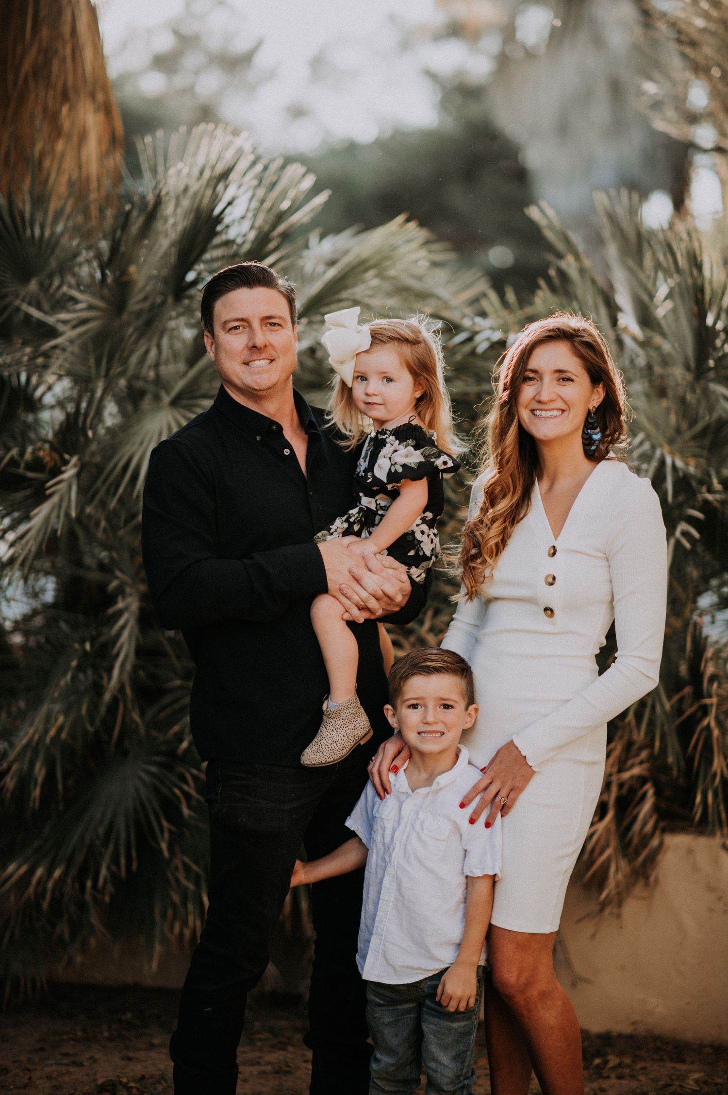 Beautiful family poses together outdoors with palm trees in background wearing coordinated black and white outfits.