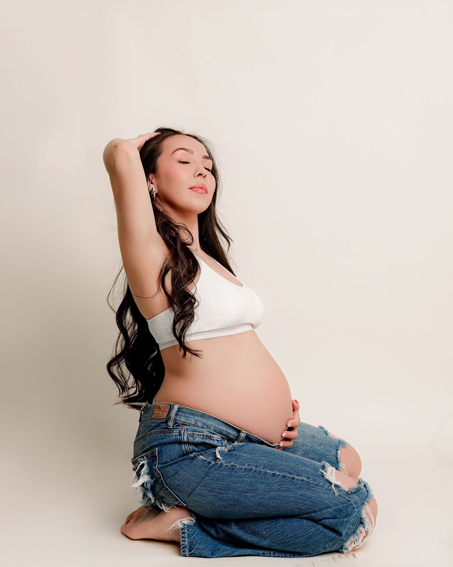 Elegant maternity portrait with flowing cream dress against textured brown backdrop.