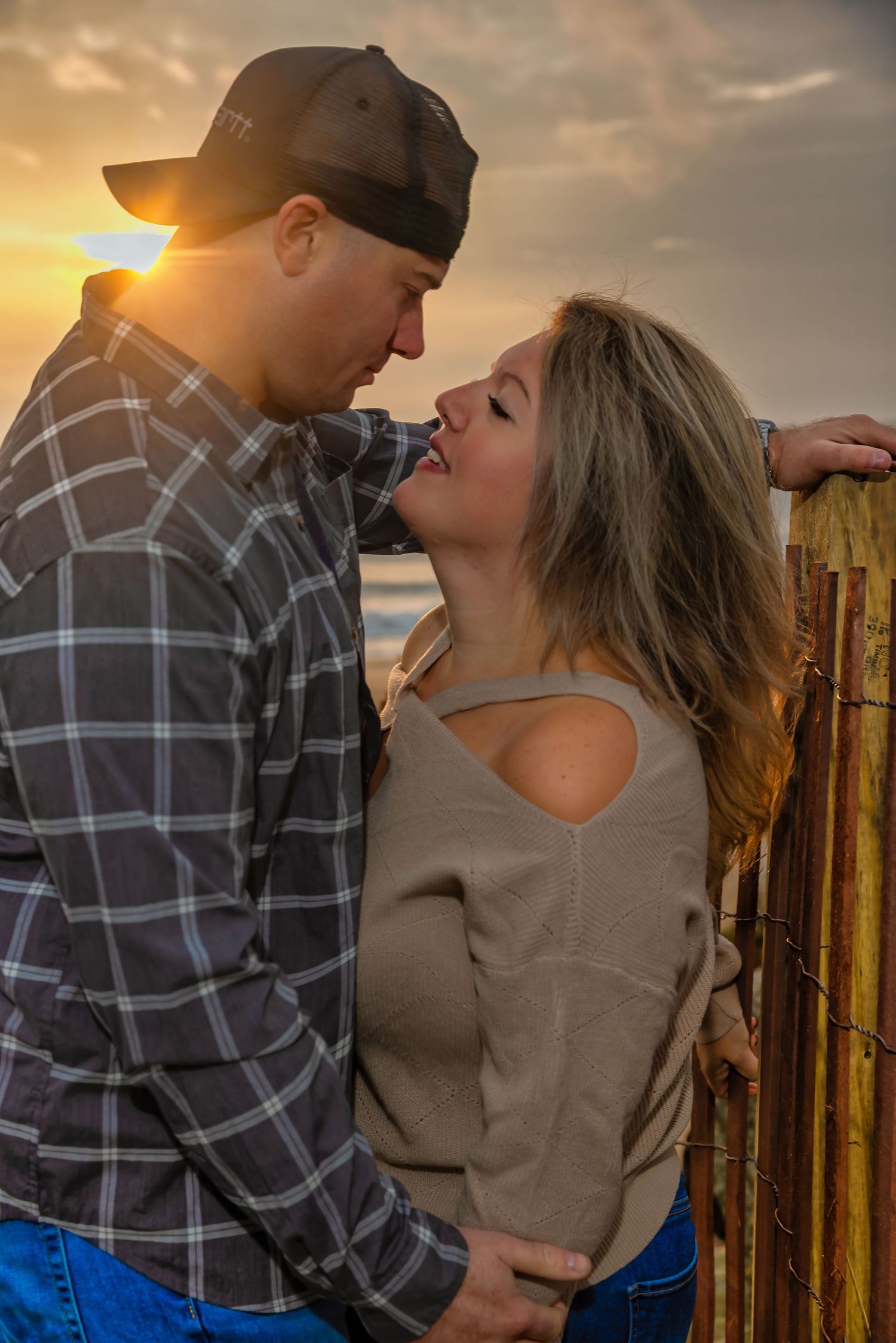 Intimate couple moment captured during golden hour at beach fence.
