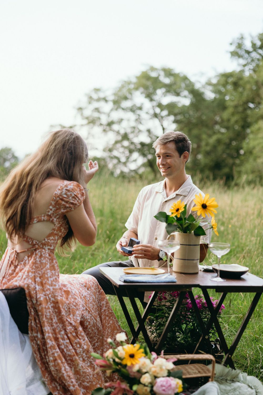 Couple enjoying romantic outdoor picnic with sunflowers and table settings in sunny meadow. Luxury Estate Wedding Photographer in NC