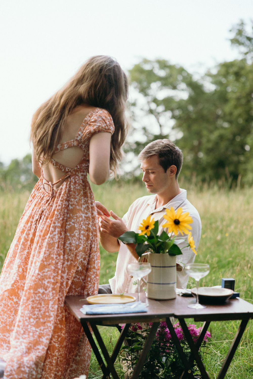 Romantic outdoor proposal scene with sunflowers and picnic setup in grassy field. Luxury Estate Wedding Photographer in NC