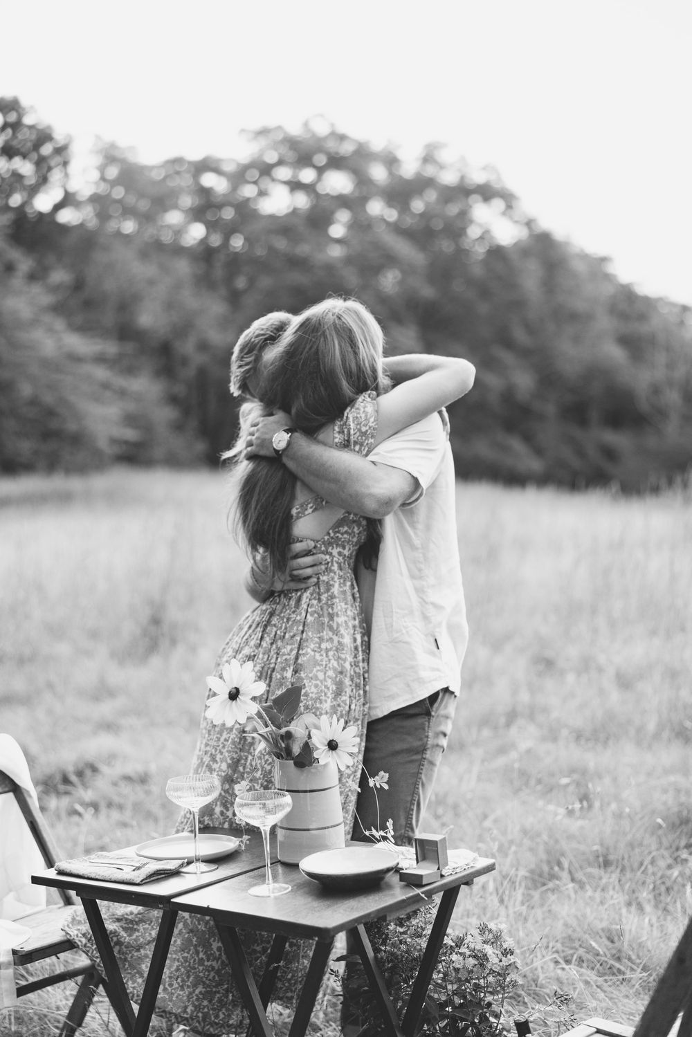 Black and white photo of couple embracing during outdoor picnic proposal. Luxury Estate Wedding Photographer in NC