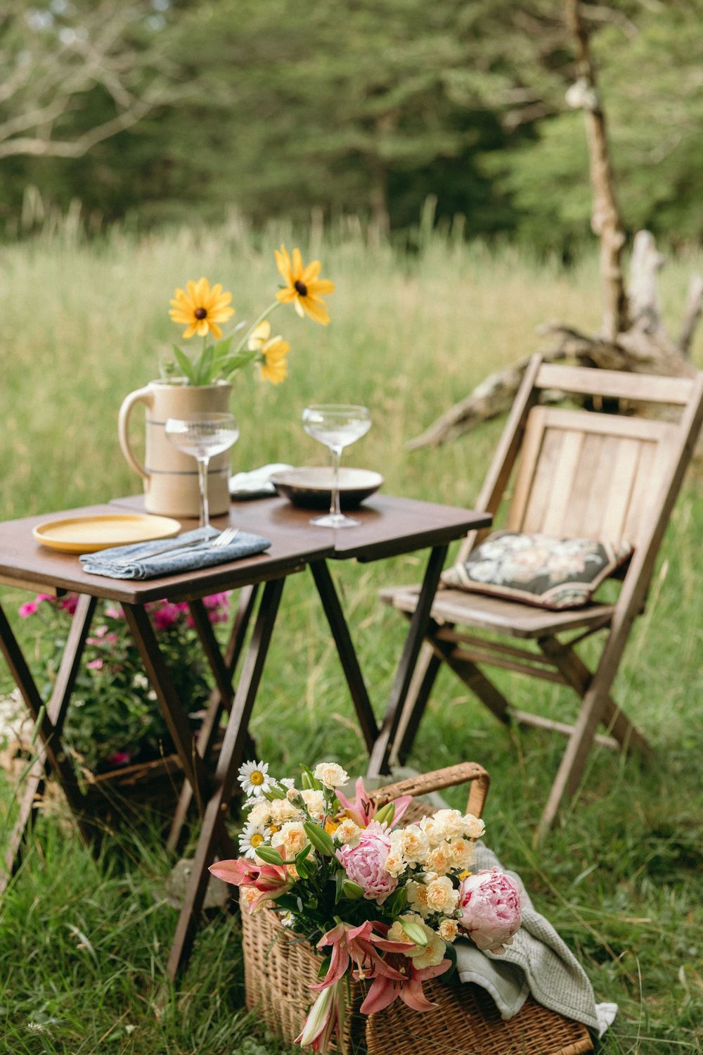 Rustic outdoor table setting with wooden chairs and colorful wildflower arrangements in a meadow. Editorial wedding photographer for NC