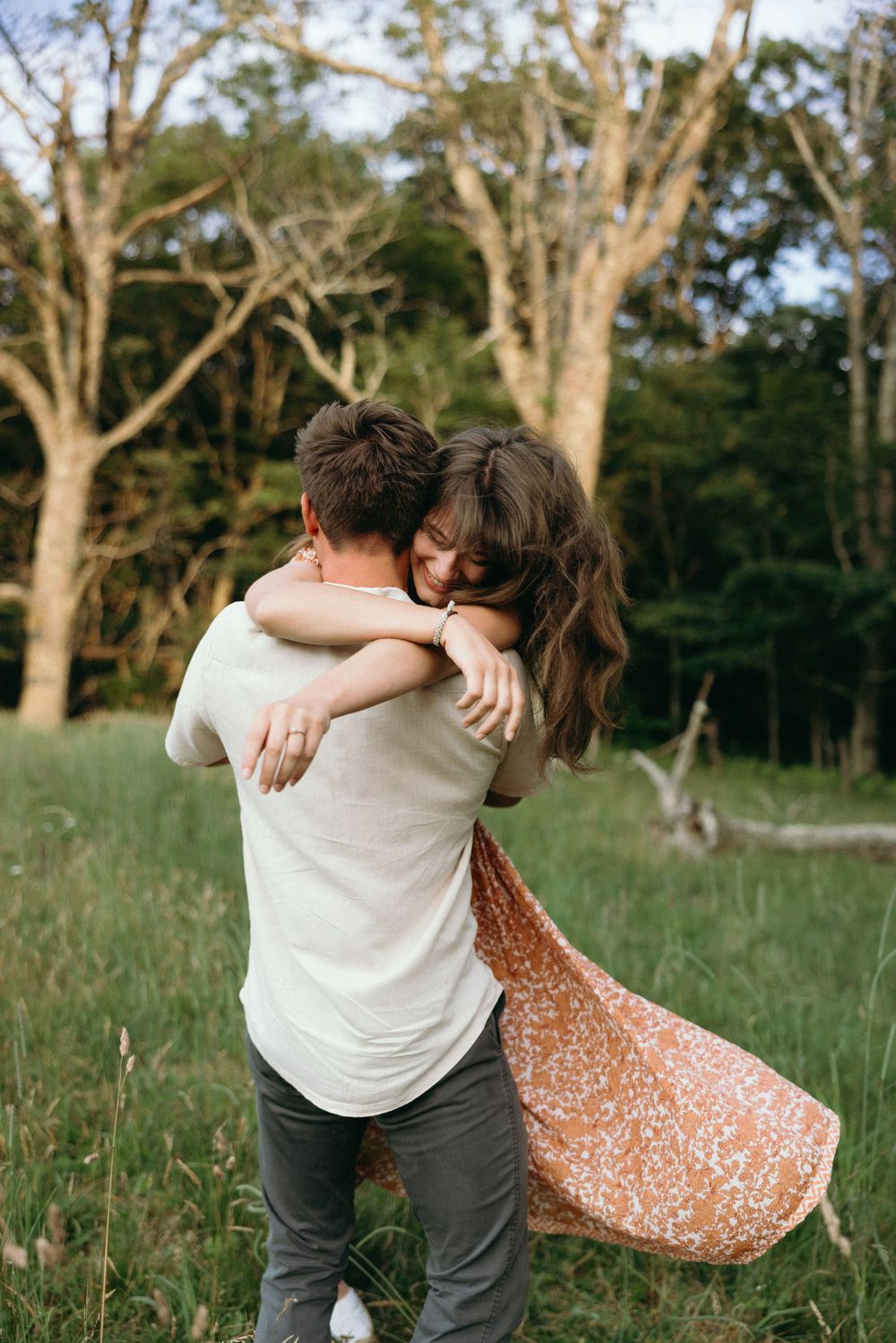Couple embracing in golden sunlight with floral dress flowing in outdoor field. Luxury Estate Wedding Photographer in NC