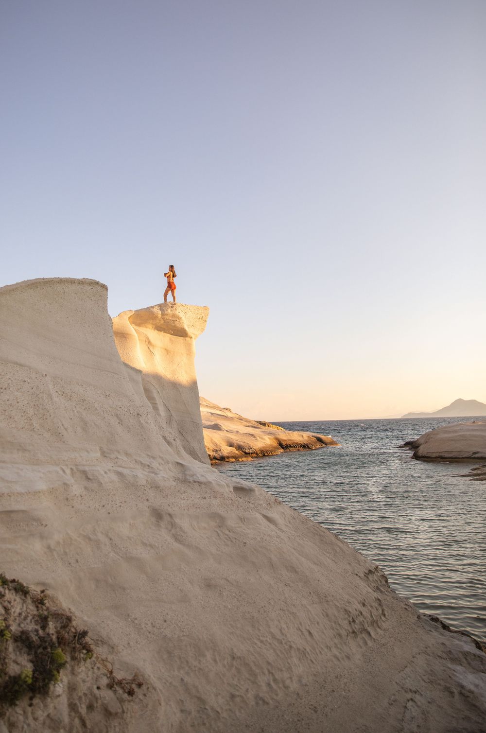 Small silhouette standing on white limestone cliff overlooking ocean at sunset.